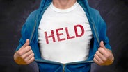 Ein Mann zeigt hinter seinem geöffneten Hemd sein T-Shirt auf dem das Wort "Held" steht. © COLOURBOX Foto: Dawesign