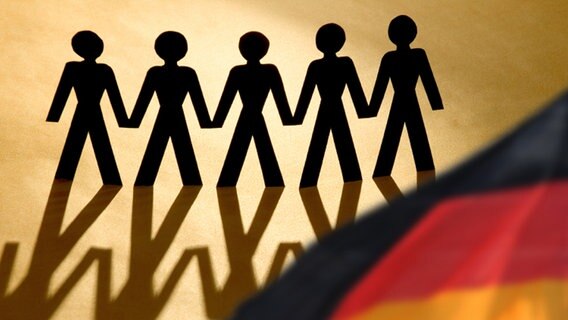 Ein Scherenschnitt von fünf Personen die sich an den Händen halten. Im Vordergrund an der rechten unteren Ecke weht eine unscharfe Deutschlandfahne. © iStockphoto abzee Foto: abzee