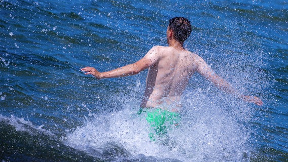 Ein Mann läuft, mit Wasser spritzend, ins Meer. © picture alliance Foto:  Jens Büttner