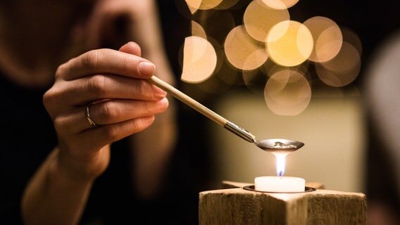 Eine Frau hält eine Löffelchen mit Blei über eine Kerze. © photocase Foto: Mickmorley