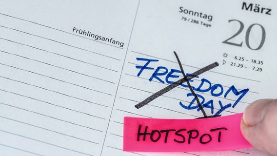 Auf einen Kalender klebt eine Person einen Zettel, auf dem "Hotspot" steht. Auf dem Kalender steht durchgestrichen: "Freedom Day" © picture alliance / Flashpic Foto: Jens Krick