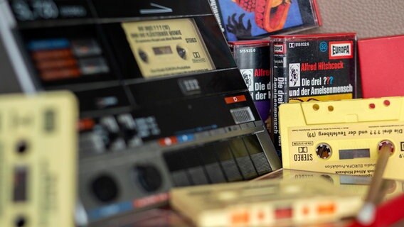 Zahlreiche Kassetten der Hörspielserie "Die drei Fragezeichen" liegen neben einem Kassettenrekorder. © picture alliance/dpa Foto: Wolfram Kastl