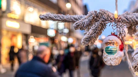 In einer Fußgängerzone hängt an einem Tannebaumzweig ein Glasanhänger in Form eines Weihnachtsmann mit Mundschutz. © picture alliance /dpa Foto: Jochen Tack