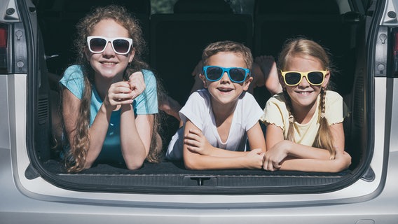 Drei Kinder mit Sonnenbrillen liegen im Kofferraum eines Autos. © photocase.de Foto: altanaka