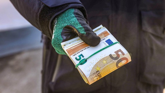 Eine Person hält ein Bündel mit Geldscheinen in einer Hand mit Handschuhen. © picture alliance / dpa-Zentralbild Foto: Tino Plunert