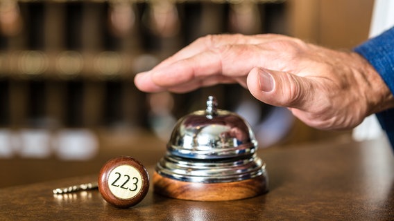 Eine männliche Hand betätigt eine Klingel an einer Hotelrezeption. © Colourbox Foto: Kzenon
