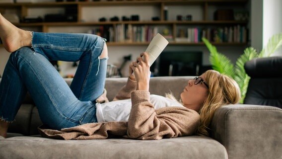 Eine junge Frau liegt lesend auf einem Sofa. © photocase Foto: Addictive Stock