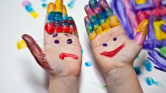 Die Hände eines Kindes sind mit einem traurigem und einem fröhlichem Gesicht bemalt © photocase.de Foto: naliaschwarz
