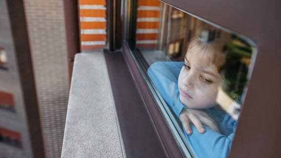 A sad girl looks out the window of a residential complex © photocase.de Photo: davidpereiras
