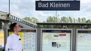 NDR Reporter Christoph Cyrulies blickt in Bad Kleinen auf das Bahnhofsschild. © NDR Foto: Sabine Frömel