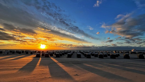 Die Sonne geht über der Ostsee unter, die Strandkörbe werfen am leeren Strand lange Schatten. © NDR Foto: Ratzie Ratzlaff aus Warnemünde