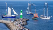 Bei der 32. Hanse Sail kreuzen historische Segelschiffe auf der Ostsee vor dem Hafen von Warnemünde und passieren die Leuchtfeuer auf den Molenköpfen. © Jens Büttner/dpa 