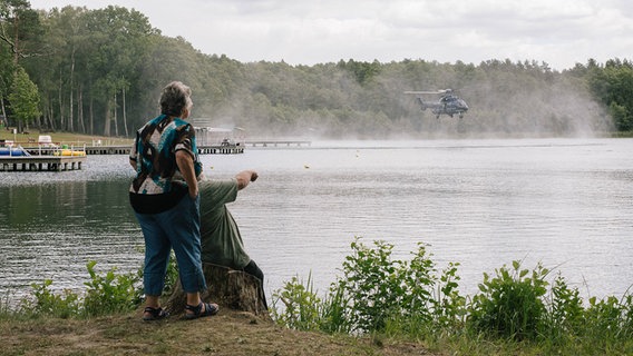 Zwei Personen sehen einem Hubschrauber bei der Wasseraufnahme zu. © imago images Foto: Michael Trammer
