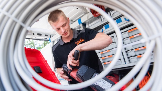 Felix Kuhlmann, Auszubildender vom Elektroinstallationsbetrieb Elektro Werk, hält Werkzeug (fotografiert durch eine Kabelrolle). © dpa-Bildfunk Foto: Julian Stratenschulte/dpa