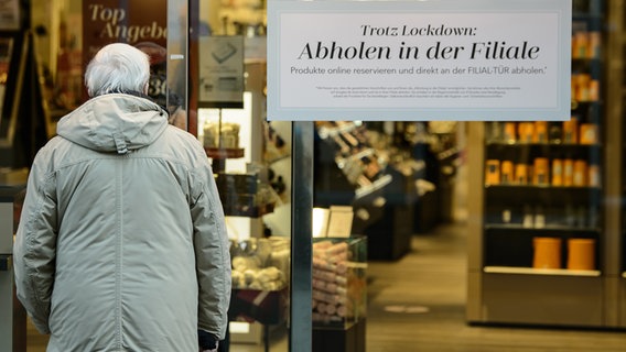 Ein älterer Mann steht vor einer Parfümerie, an deren Eingang ein Hinweis mit Aufschrift "Trotz Lockdown - Abholen in der Filiale" steht. © dpa-Bildfunk Foto: Swen Pförtner/dpa