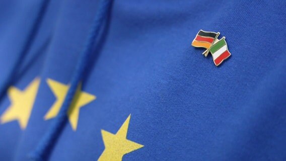 Auf einer Europaflagge sind zwei weitere Länderflaggen angebracht: Deutschland und Italien. © NDR 