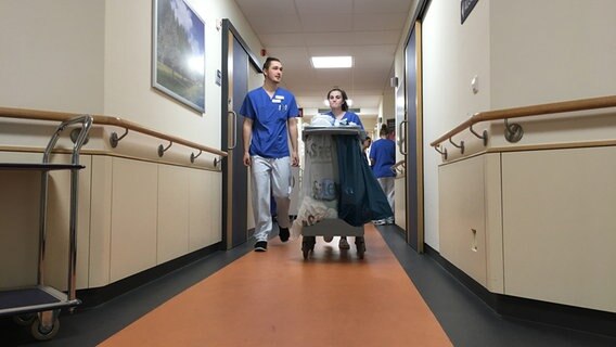 Jessica Pöpke und Jan Könke (Pflege-Azubis) schieben einen Wagen durch einen Krankenhausflur. © NDR Foto: Johannes Koch
