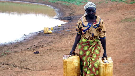 Eine Frau holt mit zwei Kanistern Wasser von einer Wasserstelle. © Wasser für Kenia 