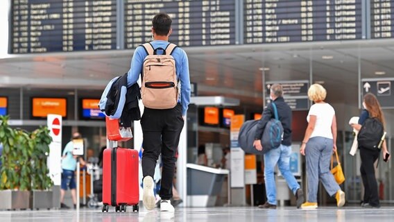 Reisende stehen an einem Flughafen vor einer Anzeigetafel. (Sybolbild) © picture alliance / Sven Simon Foto: Frank Hoermann