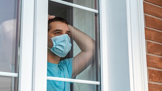 Ein Mann steht mit einem Mund·schutz am Fenster. © Colourbox 