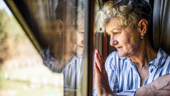 Eine ältere Frau schaut traurig aus dem Fenster © Colourbox 