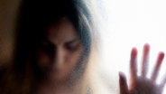 Eine Frau stützt sich mit gesenktem Blick mit der Hand gegen eine krauselige Glasscheibe. © Imago Images / Westend61 Foto: Westend61