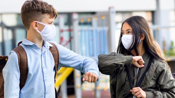 Zwei Teenager-Schüler mit Schutzmasken begrüßen sich mit einem Ellenbogen-Kick. (Themenbild) © Colourbox Foto: -