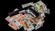 Auf vielen Geldscheinen liegt eine Pistole © picture alliance /Fotostand Foto: Radedzki
