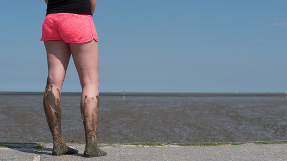 Eine Frau mit matschigen Beinen steht auf einem Weg und blickt auf das Watt. © photocase Foto: hoffi99