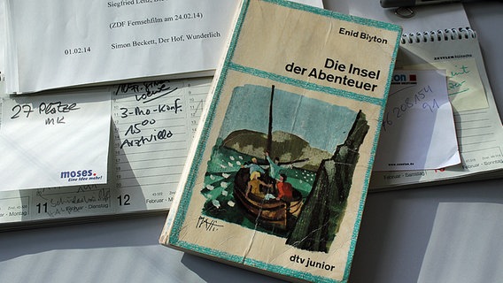 Das Buch "Die Insel der Abenteuer" liegt mit anderen Papieren auf einem Schreibtisch. © NDR Foto: Katharina Mahrenholtz