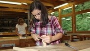 Elizabeth steht in einer Werkstatt und raspelt einen Salatlöffel im Werkunterricht. © NDR Foto: Beke Schulmann