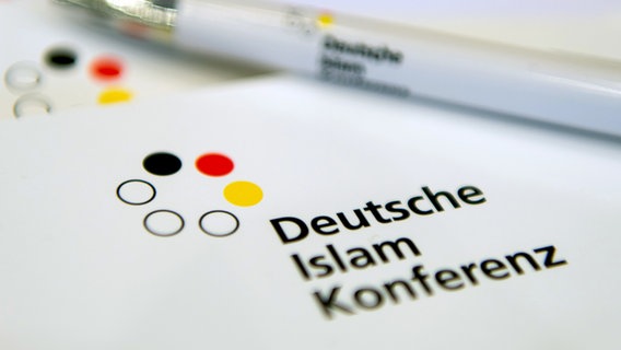 Ein Kugelschreiber liegt auf dem Logo der Deutschen Islam Konferenz © Sebastian Gollnow/dpa 