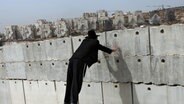 Ein ultraorthodoxer Jude schaut über eine Mauer auf die israelische Siedlung Modi'in Illit im Westjordanland. © picture-alliance/dpa | Nati_Shohat 