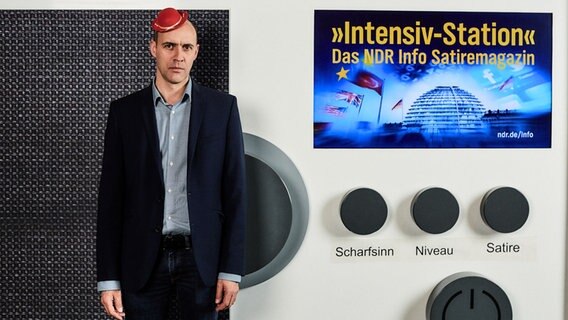 Moderator Ocke Bandixen steht vor einem riesigen Radio. Auf dem Kopf trägt er einen viel zu kleinen roten Hut. © NDR Foto: Hendrik Lüders