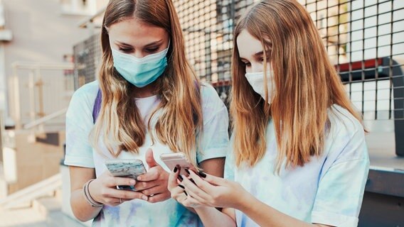 Zwei Jugendliche mit Mund-Nasen-Schutz blicken auf ihre Smartphones © photocase.de Foto: przemekklos