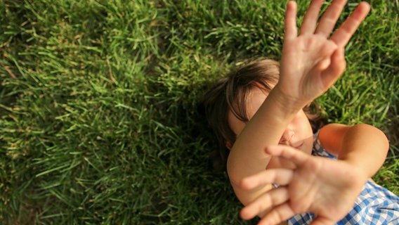 A child is lying on the grass with his hands in the air and in front of his face.  © Photo: LP