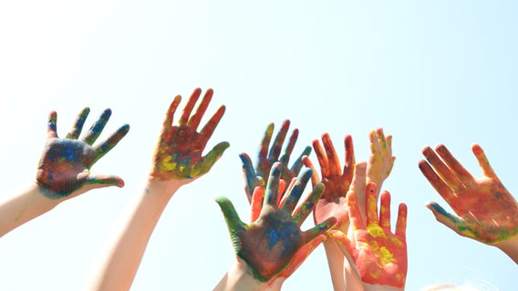 Mit Farbe angemalte Kinderhände vor blauem Himmel. © rosabrille 