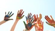 Mit Farbe angemalte Kinderhände vor blauem Himmel. © rosabrille 