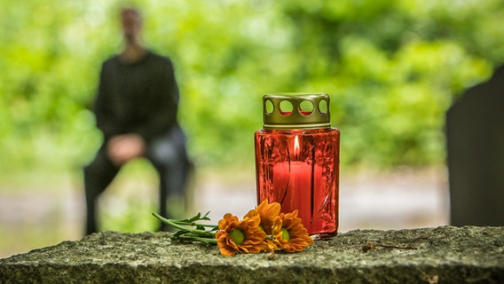 Auf einem Grabstein steht ein rotes Grablicht © picture alliance / dpa-tmn Foto: Christin Klose