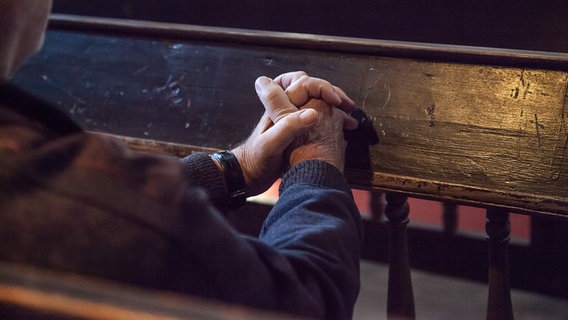 Ein Mann sitzt in einer Kirchenbank und betet. © Kirche im NDR Foto: Christine Raczka