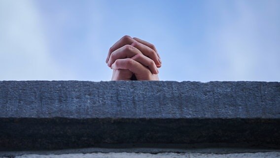 Gefaltete Hände stützen sich auf einer Mauer auf. © dpa-Zentralbild Foto: Annette Riedl