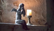 Eine weinender Engel sitzt neben einer brennenden Kerze. © Kirche im NDR / Christine Raczka Foto: Christine Raczka