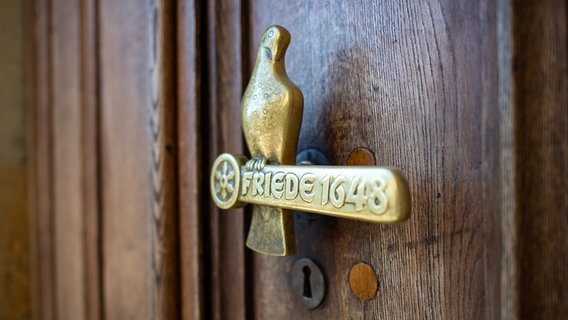 An der Eingangstür zum Historischen Rathaus in Osnabrück ist eine Türklinke aus Bronze in Form einer Taube und der Aufschrift: "Friede 1648" zu sehen. © dpa Foto: Guido Kirchner