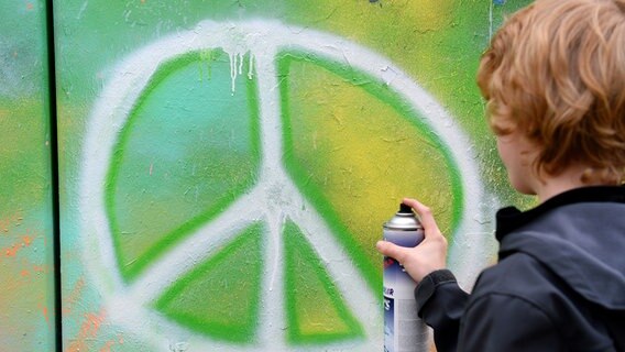 Ein Junge sprüht das Friedenssymbol auf eine Wand. © picture alliance / Frank May Foto: Frank May