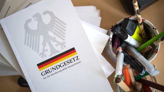 Eine Ausgabe des Grundgesetzes der Bundesrepublik Deutschland liegt neben Schreibutensilien. © ZB/dpa Foto: Monika Skolimowska