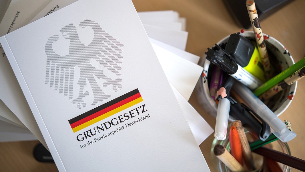 Eine Ausgabe des Grundgesetzes der Bundesrepublik Deutschland liegt neben Schreibutensilien.