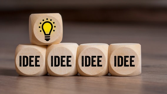 Vier Würfen mit der Aufschrift "Idee", einer mit einer leuchtenden Glühbirne liegen auf einem Tisch. © colourbox Foto: stockwerk-fotodesign