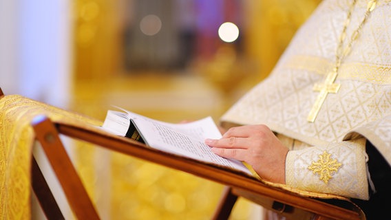 Die Hand eines Geistlichen liegt auf einer Bibel. © Colourbox 
