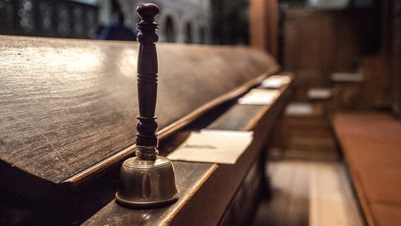 Eine Glocke steht vor einer leeren Kirchenbank. © Kirche im NDR Foto: Christine Raczka