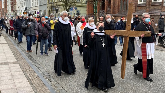 Mehrere Geistliche tragen ein hölzernes Kreuz durch die Lübecker Innenstadt, dabei folgen ihnen zahlreiche Gläubige. © NDR Foto: Linda Ebener